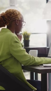 Vertical video: African american woman checking annual report on pc, looking at company results and research for growth. Business manager analyzing statistics to increase company profit in workplace.