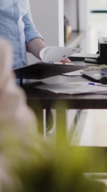 Vertical video: Professional employee analyzing company data on files, working with investment plan for successful growth. Female worker checking analytics and statistics on papers, annual report.