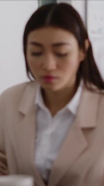 Vertical video: Young employee dealing with headache and working on computer, rubbing temples and feeling worried about pain. Female entrepreneur having painful migraine at desk, work under pressure.