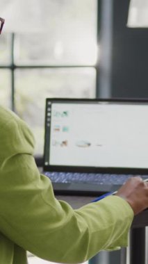 Vertical video: Business woman looking at annual report on laptop, planning corporate investment for marketing development. Startup worker checking data analytics on pc, taking notes on documents.