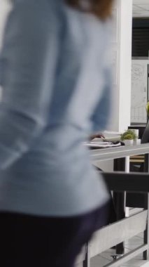 Vertical video: African american assistant answering landline phone call and talking to manager about business solutions. Corporate employee using office cord telephone in startup coworking space.