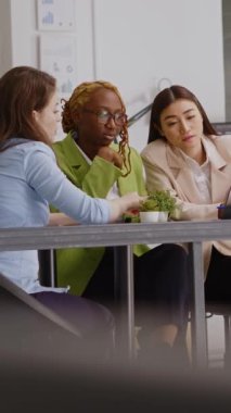 Vertical video: Diverse coworkers analyzing statistics on papers and pc screen, showing executive data report in briefing meeting. People doing teamwork discussing about new development strategy