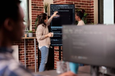 Team of coders talking about algorithms in front of big screen, analyzing html script language. Software developers discussing database on terminal window working in it programming agency