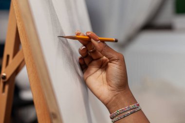 Talented unrecognizable woman hand holding professional drawing pencil to make artwork on canvas. Close up of unidentified female artist making hand drawn on easel in home art studio.
