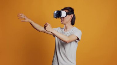 Modern person using vr glasses for 3d simulation, enjoying cirtual reality on interactive headset. Happy cool male model having fun with goggles and innovative gadget, orange background.