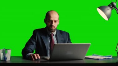 Entrepreneur looking at data on isolated greenscreen, and working on laptop. Young businessman in suit and tie standing over blank mockup and chroma key background, white collar.