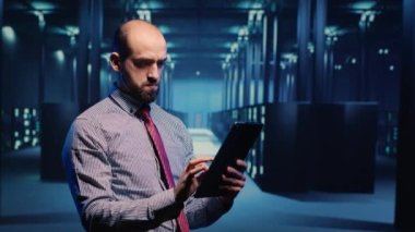 Data center IT engineer standing in server room with rack cabinets, inspecting cloud computing big data service. System administrator running networking backup on tablet, artificial intelligence.