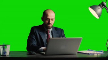 Executive manager using laptop over green screen backdrop, using computer at desk. Confident corporate employee posing on blank chroma key template, isolated copyspace background.