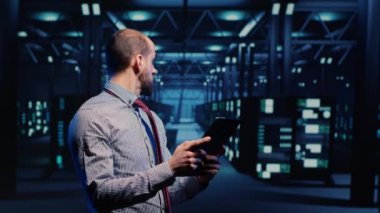 Information security officer working in data center with tablet, analyzing server rack cabinets in render farm. IT support specialist inspecting cloud computing system, ai concept. Tripod shot.