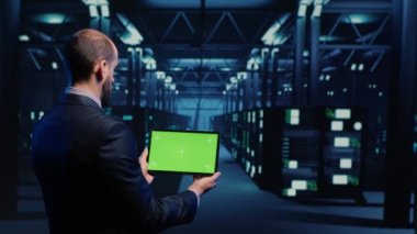 System engineer checking green screen display on tablet, running mainframe diagnostics in data center. IT administrator using copyspace display with blank chroma key, ai concept. Tripod shot.
