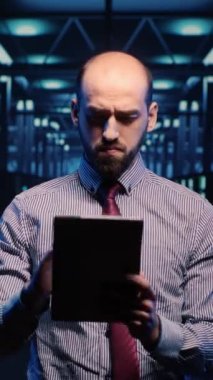 Dikey video: IT yöneticisi teknik destek operatörü sunucu odasında büyük verileri kontrol ediyor, dijitalleştirme planlıyor. Yapay zeka ve sunucuyla çalışan bir destek uzmanı. Üçayak atışı