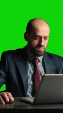 Vertical video: Businessman over greenscreen feeling tired and stressed, sitting laid back at desk. Team leader working over chroma key backdrop with isolated mockup template, exhausted adult.