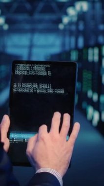 Vertical video: Support specialist checking server computers on tablet, planning mainframe system backup in server room. Information security officer running diagnostics, cloud computing. Handheld
