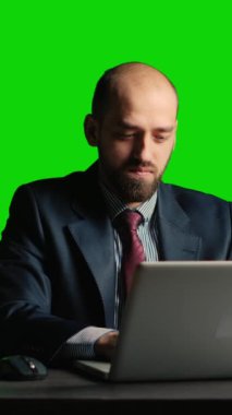 Dikey video: Yönetici yönetici masadaki bilgisayarı kullanarak yeşil ekran arkaplanı üzerinde laptop kullanıyor. Boş kroma anahtar şablonu, izole edilmiş telif alanı arka planı üzerinde duran kendinden emin şirket çalışanı.