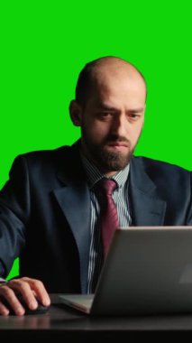 Vertical video: Office employee answering phone call on green screen, posing over isolated chroma key template in office. Young manager using smartphone on blank copyspace mockup backdrop at desk.