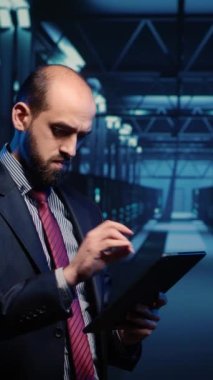 Vertical video: IT engineer using tablet in high tech server room, planning networking computer system. Database admin activating hardware server in data center, mainframe computer processor storage.