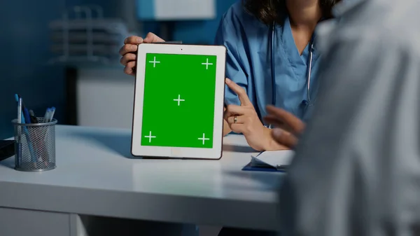 Assistant showing tablet computer with green screen template to physician while discussing patient medical expertise during checkup visit. Clinical staff working late at night in hospital office