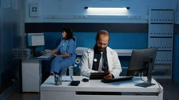Caucasian physician doctor holding tablet computer searching for patient disease expertise before start planning health care treatment in hospital office. Medical team working late at night