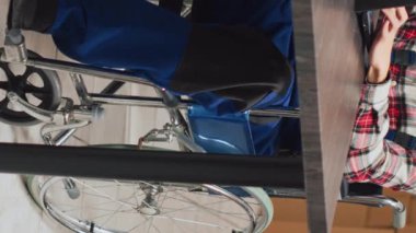 Vertical video: Man with chronic disability using laptop in warehouse, checking stock of merchandise for logistics and management. Young employee working in disability friendly space, supply chain.