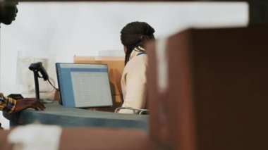 Depo çalışanı bilgisayarda hisse senedi lojistiği planlıyor, ambardaki karton paketlerde ürünlerle çalışıyor. Depoda eşyalar ve paketlerle çalışan bir kadın..