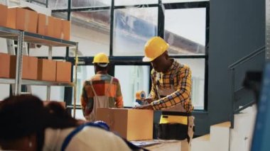 African american men packing products in boxes, using warehouse tools to plan retail shipment in storage room. Male employees working with products logistics, shipping merchandise. Handheld shot.