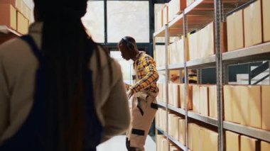 Storehouse worker dancing and singing at work, having fun with dance moves in storage room. Young adult preparing products or goods in packages, carton boxes on racks. Handheld shot.