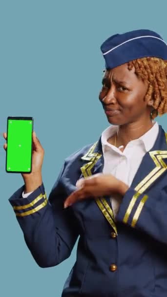 垂直视频 非洲裔美国妇女手持带有绿色屏幕的电话 在演播室中展示带有空白复制空间的孤立显示 女性客机在蓝屏上看模型模板 — 图库视频影像