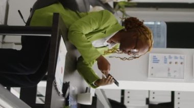 Vertical video: Female office worker using phone at corporate job, sitting at desk planning company investment. Executive assistant browsing social media on smartphone, working on business solutions.