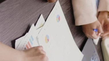 Vertical video: Diverse women analyzing data statistics on documents, looking at papers to find new business solutions in briefing meeting boardroom. Group of employees discussing marketing vision