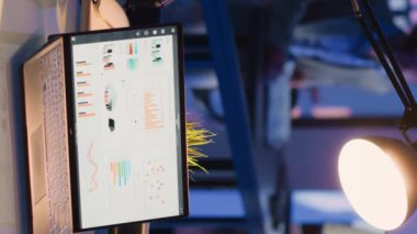 Vertical video: Startup worker typing financial data report on screen, looking at business diagrams and graphs for corporate investment. Young employee working overtime in office, planning progress.