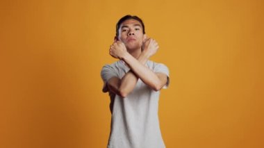 Asian person showing x shape gesture with hands, expressing refusal and disagreement. Young male model showing no symbol and rejection, refusing to listen over orange backdrop.