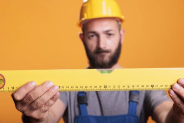 Focused foreman expert looking at construction leveler before working on refurbishment project, studio shot. Handyman builder carrying water level tool or ruler to work on renovation.