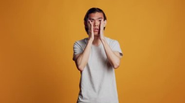 Sick male model dealing with painful headache, feeling tired and stressed on camera. Young ill person suffering from serious migraine, acting unhappy in studio and rubbing temples.