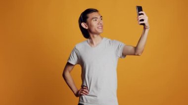 Happy guy taking pictures and acting carefree, smiling and posing for photos on mobile phone. Young cheerful model taking images on smartphone, posting on social media page, hipster look.
