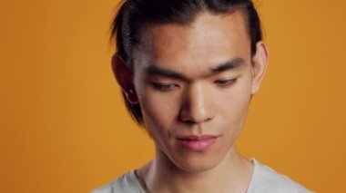 Happy man smiling and being excited on camera, posing over orange background with confidence. Young asian model acting positive and friendly in studio, hipster with athletic casual style.