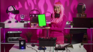 Artist holding vertically green screen chroma key tablet computer with isolated display, playing stereo sounds with electronics using professional turntables. Musician having fun in night club