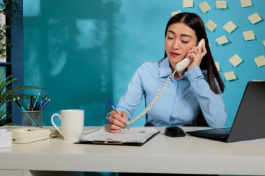 Corporate asian female employee talking with work colleague on the phone reviewing statistical report to present to management. Professional woman marketing expert reviewing paperwork.