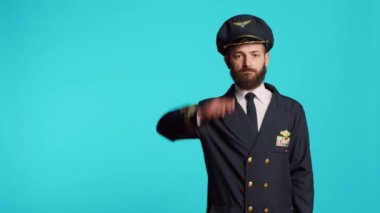 Male aviator doing military salute over blue backdrop, showing respect for army. Airplane captain serving flying industry as aviation worker, working on commercial flights and transportation.