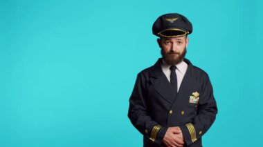Male plane captain wearing airline uniform and posing in studio, having professional occupation. Young adult working as pilot to fly airplane, being cheerful and positive on camera.