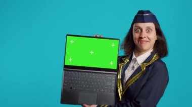 Positive aviator showing laptop with greenscreen, using chroma key blank copyspace on wireless computer. Young woman in uniform looking at isolated mockup template and chromakey.