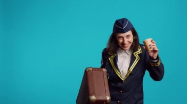 Smiling air hostess carrying suitcase to leave for work, drinking coffee and getting ready for departure. Stewardess preparing to fly on airplane, holding briefcase and feeling confident.