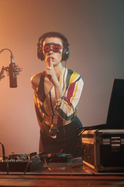 Cool performer showing mute secrecy sign, advertising secret and privacy before using turntable to mix records. Producing music at DJ mixer and doing hush confidential symbol in studio.