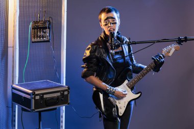 Ecstatic artist screaming loud in studio and singing heavy metal music, using electric guitar to play song. Alternative rock singer doing live performance with leather jacket, playing instrument.