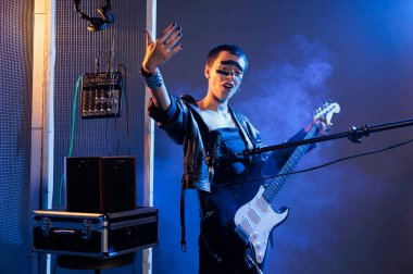 Woman artist with crazy make up creating cool vibe, doing live performance with rock and heavy metal music. Stylish solo musician with guitar doing concert and screaming loud, studio with smoke.