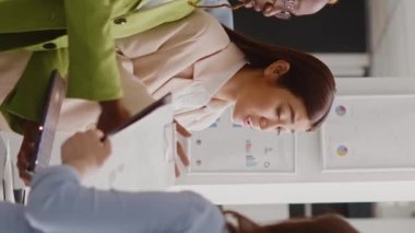Vertical video: Multiethnic startup team analyzing business data in office and using investment plan with research and analytics. Young women brainstorming new solutions in coworking space, briefing