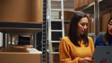 Yönetim ekibi raflara mal yerleştiriyor, depo alanındaki stok lojistiği planlamak için dizüstü bilgisayar kullanıyor. Raflardaki perakende ürün paketlerine bakan kadın çalışanlar, iş planı.