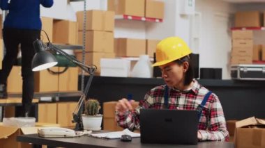 Warehouse employee looking at stock logistics on pc, checking quality of products before planning shipment. Young man working on merchandise products, using laptop for inventory. Handheld shot.