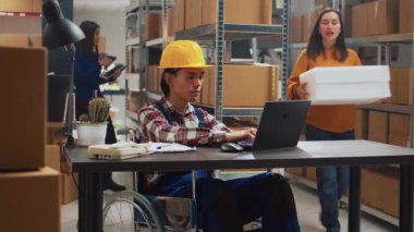 Young man in wheelchair looking at stock supplies, checking merchandise in boxes with female worker. Asian adult with impairment planning business development in storage room.