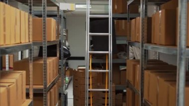 Small business warehouse in storage room filled with carton packs, office space with laptop for product inventory or logistics. Empty depot with stacks of merchandise for stock distribution.