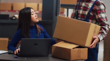 Young man analyzing boxes of supplies in storehouse to help female employee with financial planning and business development. Team of colleagues working on inventory and shipment. Handheld shot.